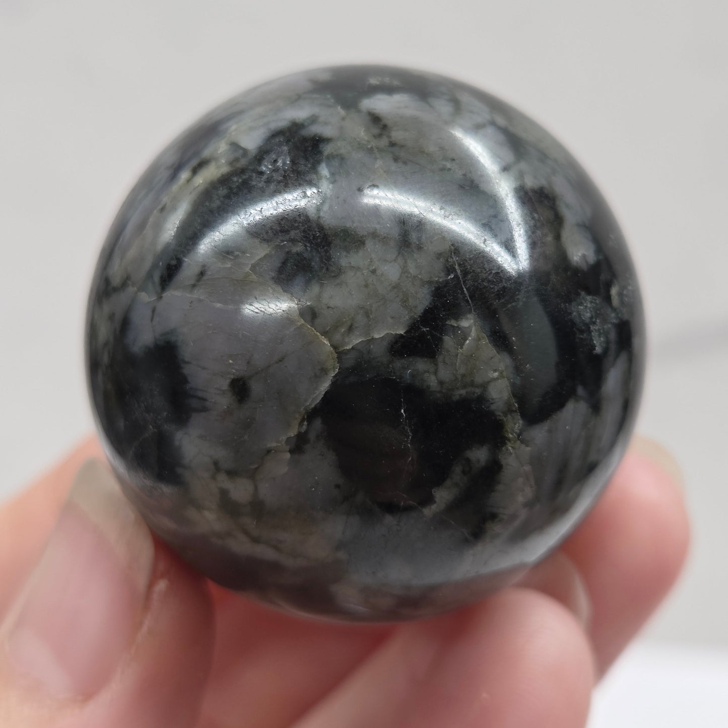 Person holding a dark marbled crystal sphere against a neutral background