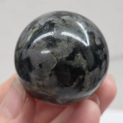 Person holding a dark marbled crystal sphere against a neutral background