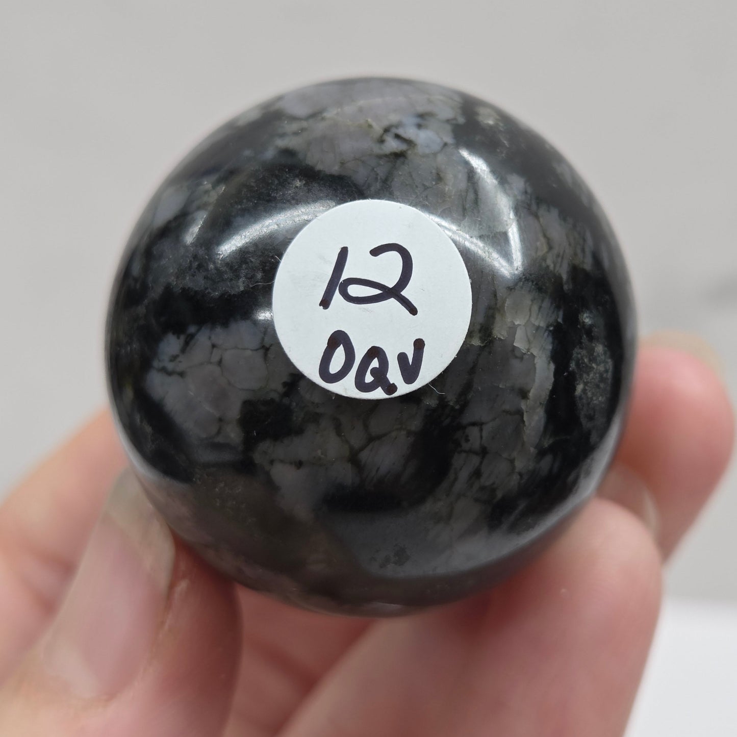 Person holding a dark marbled crystal sphere against a neutral background