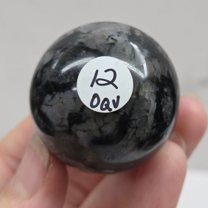 Person holding a dark marbled crystal sphere against a neutral background