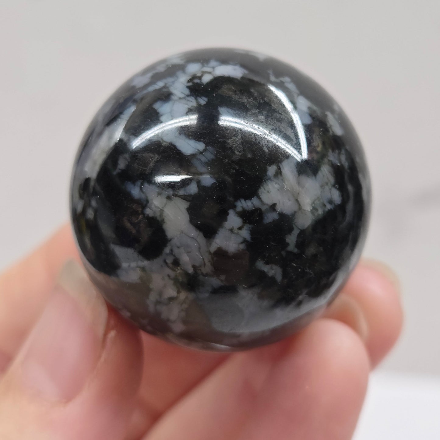 Person holding a dark marbled crystal sphere against a neutral background