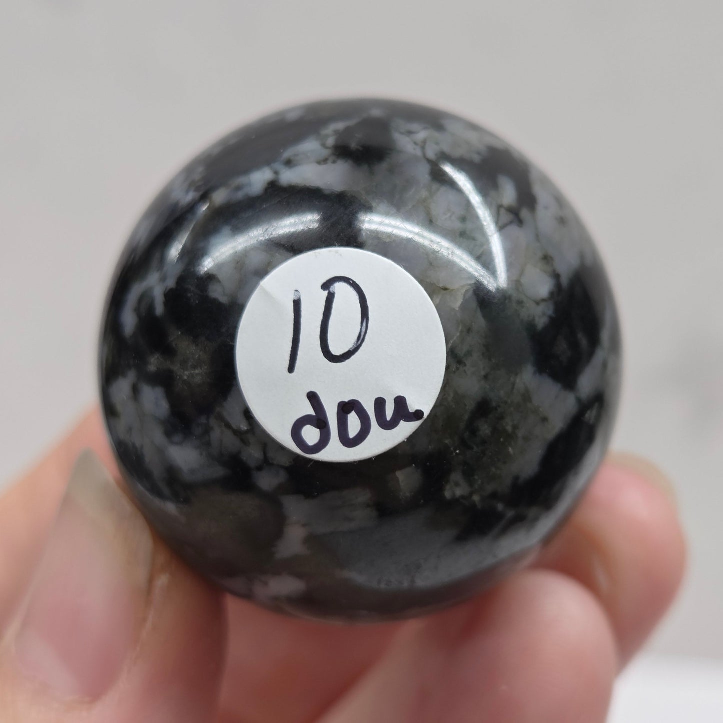 Person holding a dark marbled crystal sphere against a neutral background