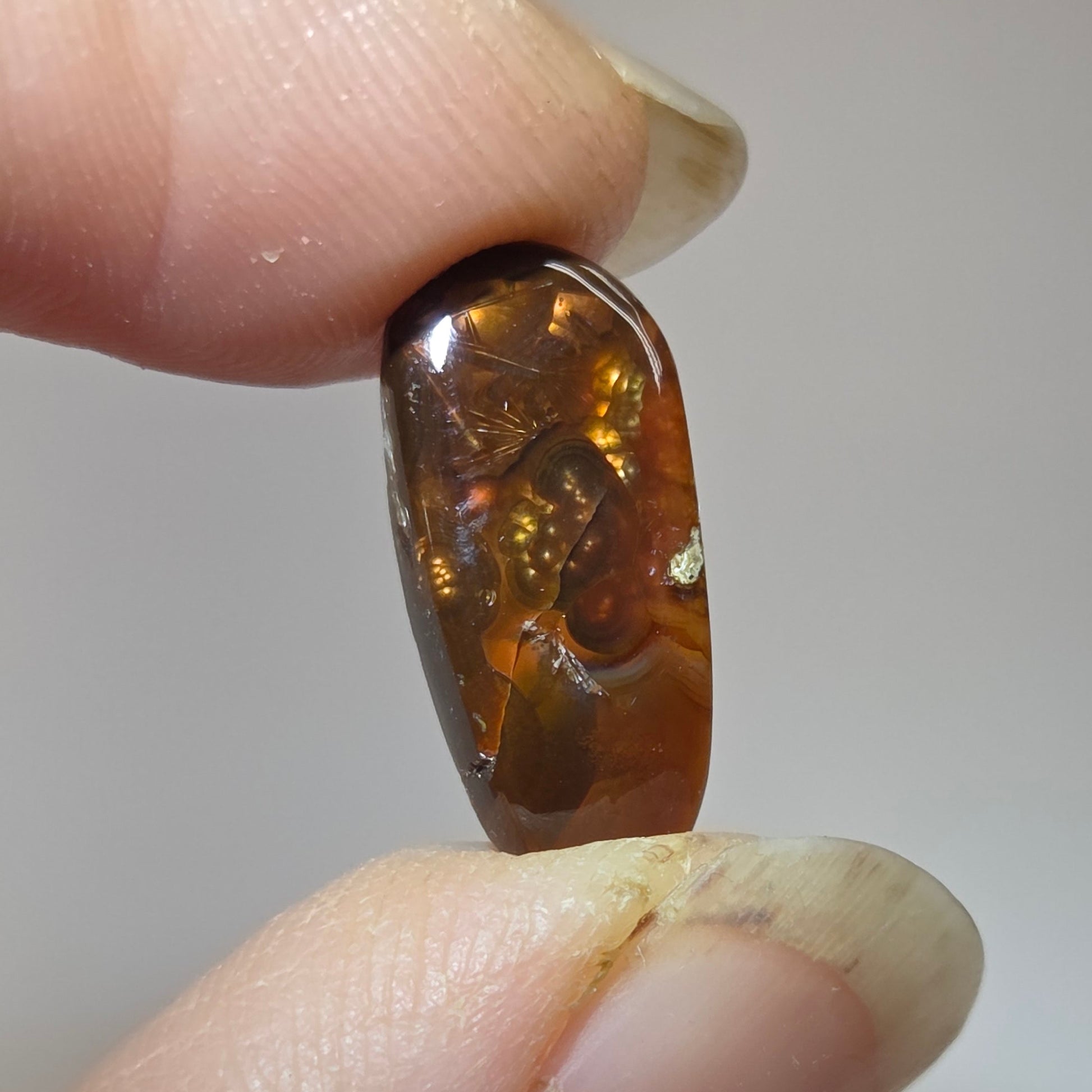 Fire Agate stone held between two fingers against a neutral background