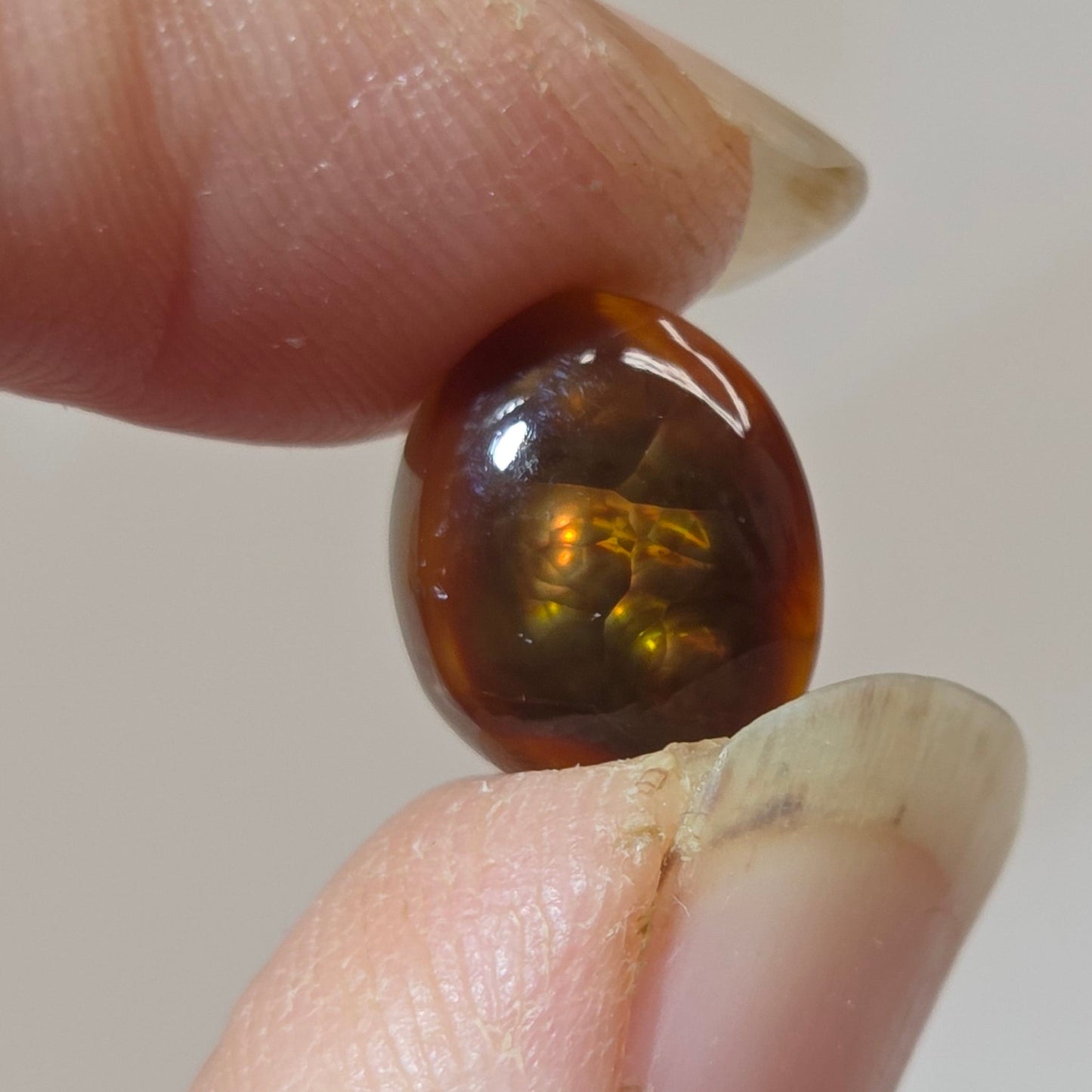 Fire Agate stone held between two fingers against a neutral background