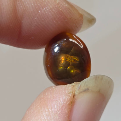 Fire Agate stone held between two fingers against a neutral background