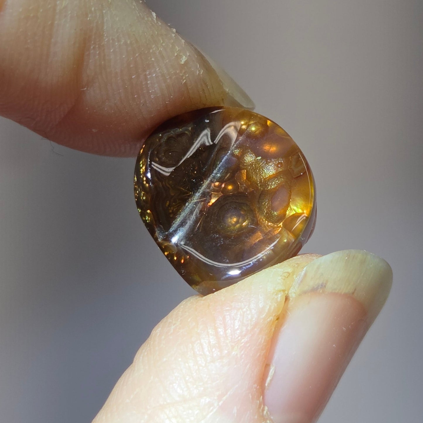 Fire Agate stone held between two fingers against a neutral background