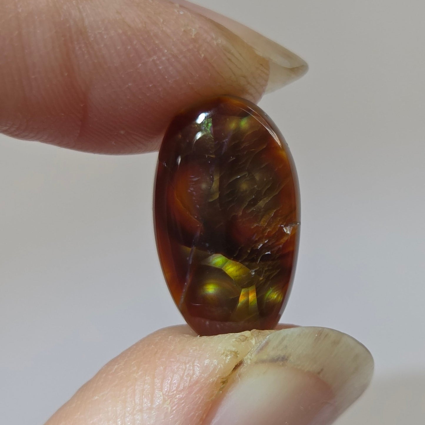 Fire Agate stone held between two fingers against a neutral background