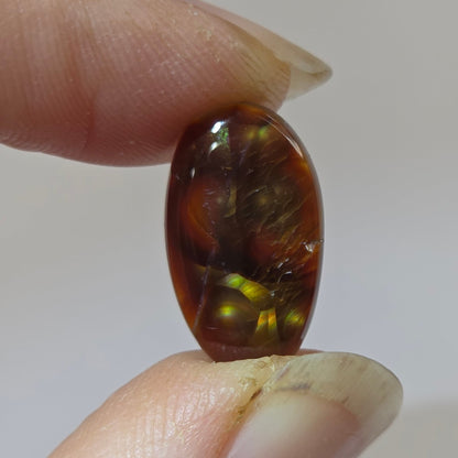 Fire Agate stone held between two fingers against a neutral background
