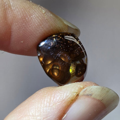 Fire Agate stone held between two fingers against a neutral background