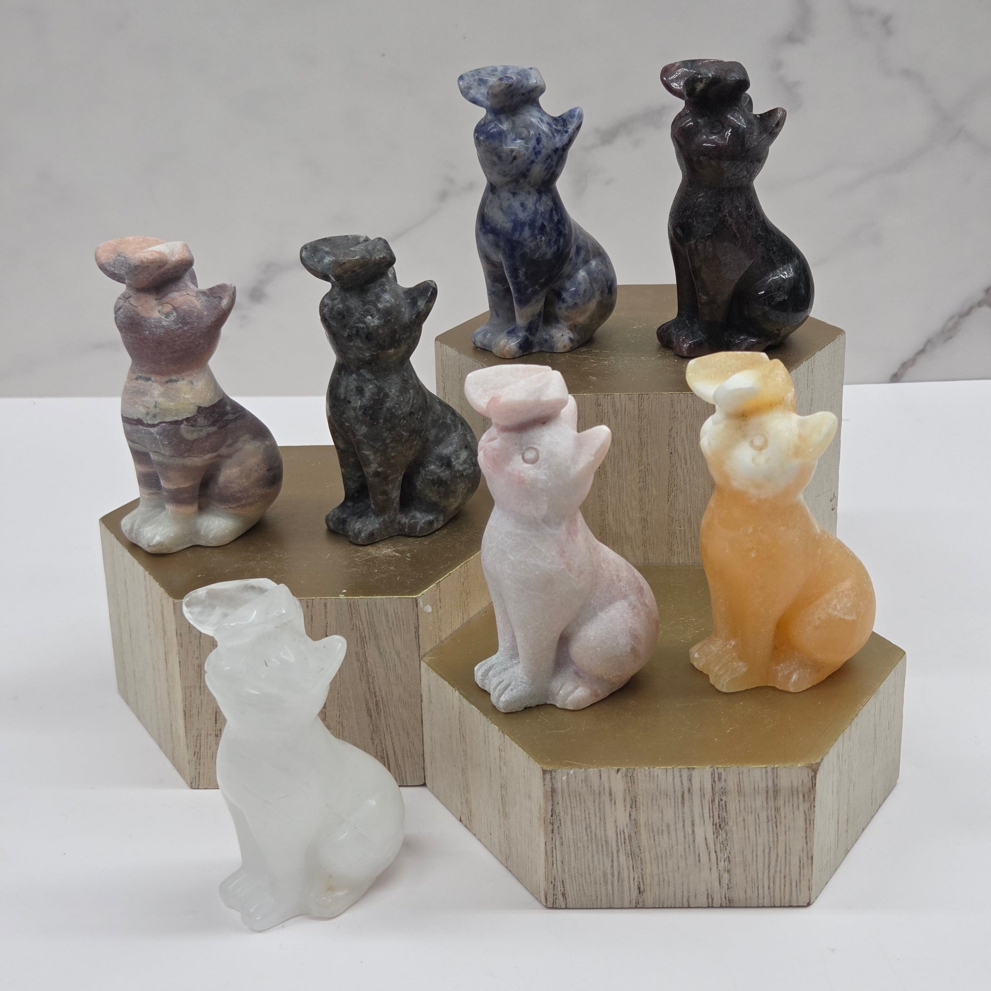 Set of small cat carvings, each with a butterfly on their nose, on a wooden stand against a marble background
