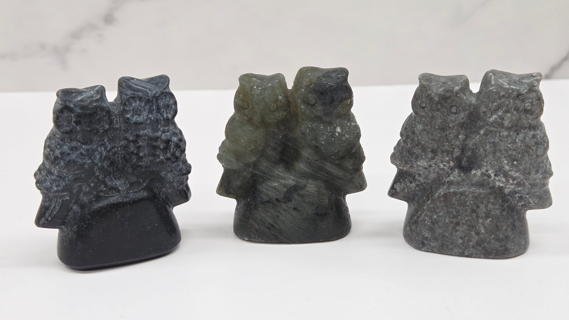 Three crystal carvings of owls on a white surface with a light gray background