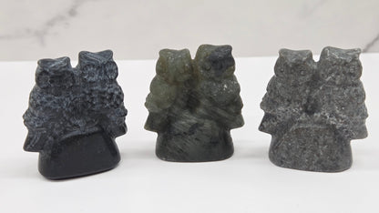 Three crystal carvings of owls on a white surface with a light gray background