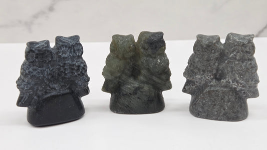Three crystal carvings of owls on a white surface with a light gray background