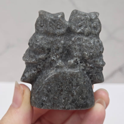 Hand holding a gray stone carving of  two owls against a light background