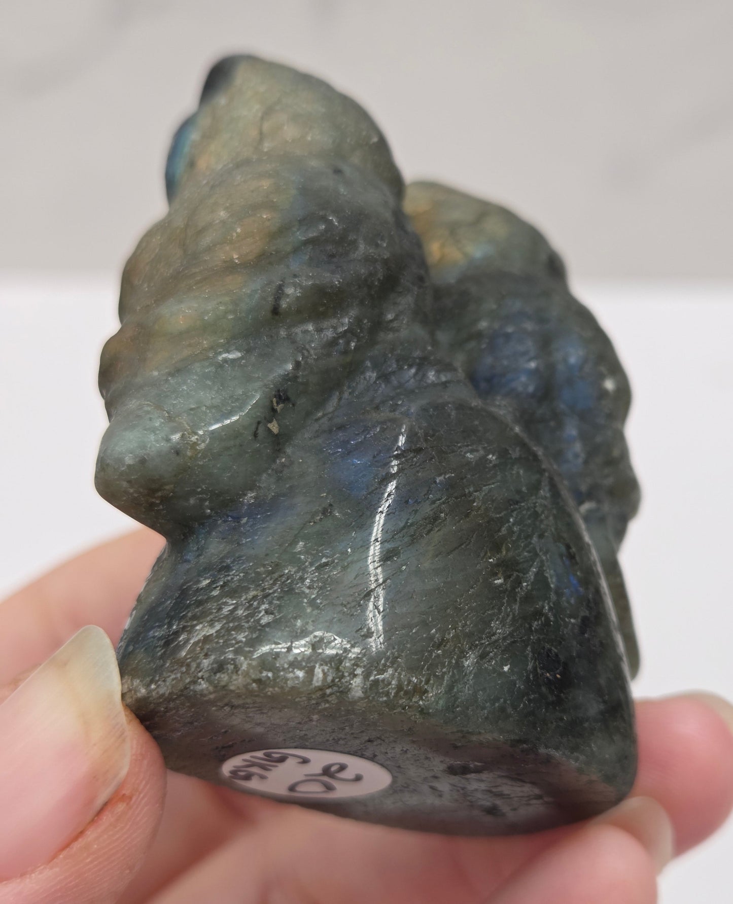 Hand holding a carved labradorite stone of two owls against a neutral background