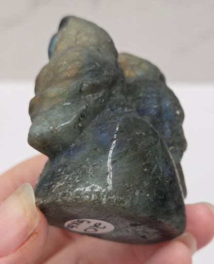 Hand holding a carved labradorite stone of two owls against a neutral background
