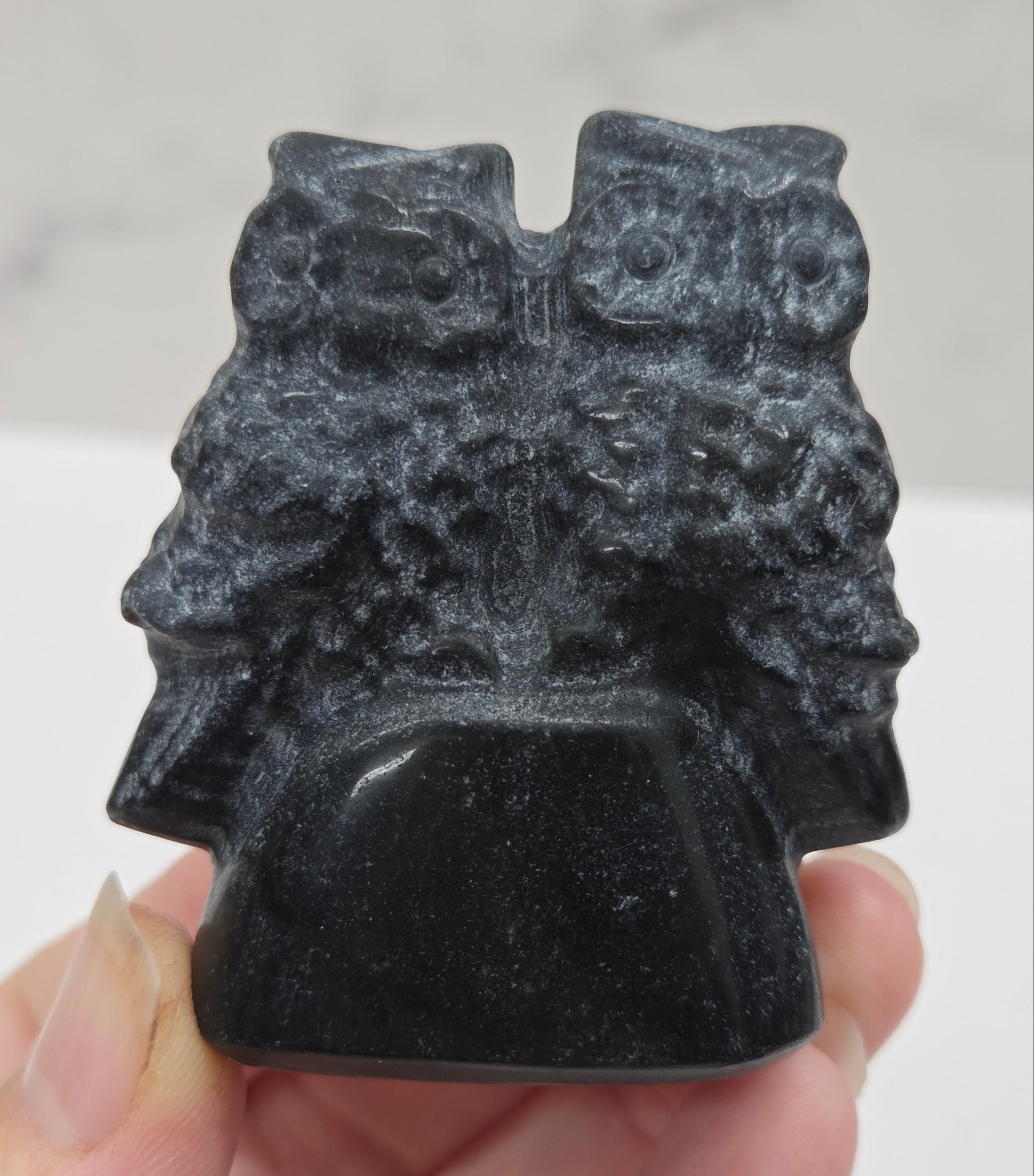 Hand holding a carved obsidian stone of two owls against a neutral background
