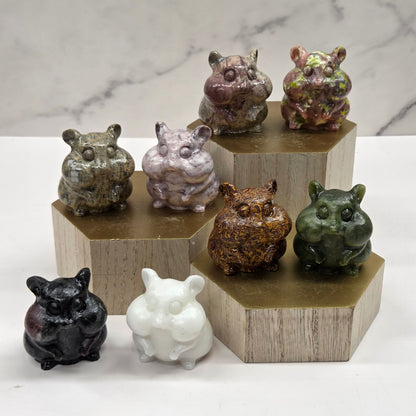 Crystal carvings of chipmunks in a variety of materials and colors on a wooden block against a marble background