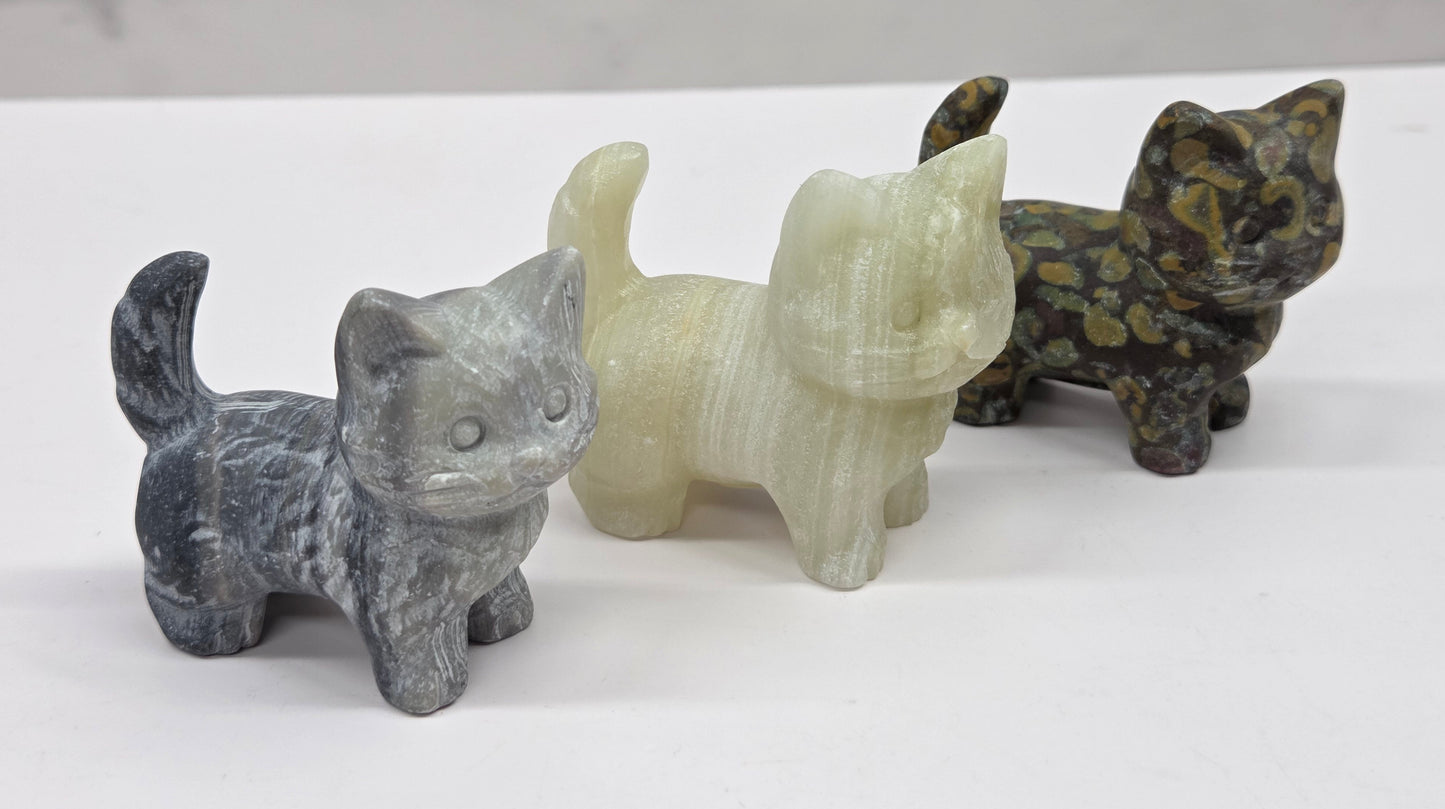 Three stone cat figurines of different colors on a white surface with a marble background.