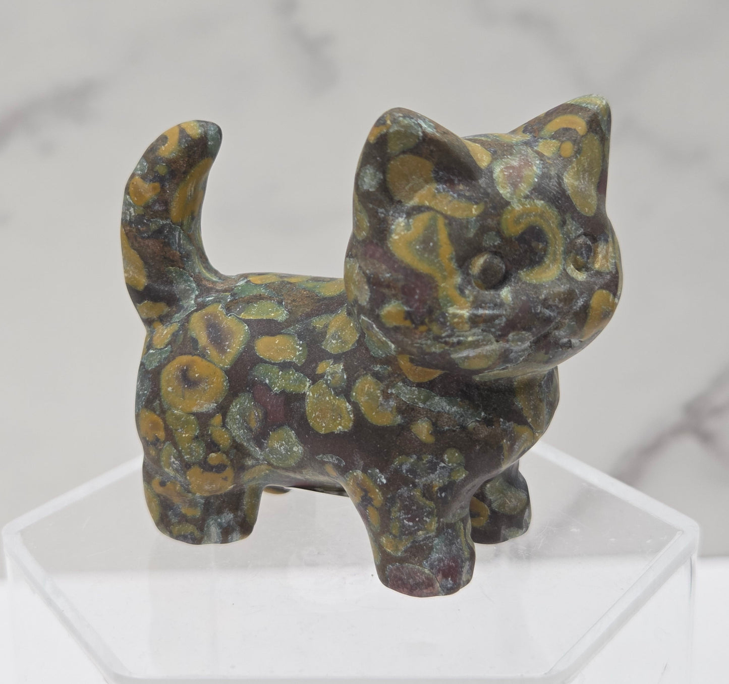 Decorative stone cat figurine on a clear stand with a marble background
