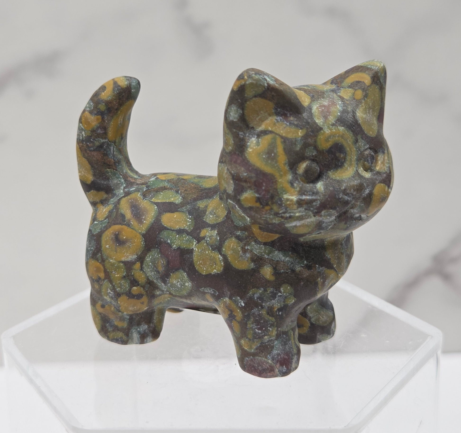 Decorative stone cat figurine on a clear stand with a marble background