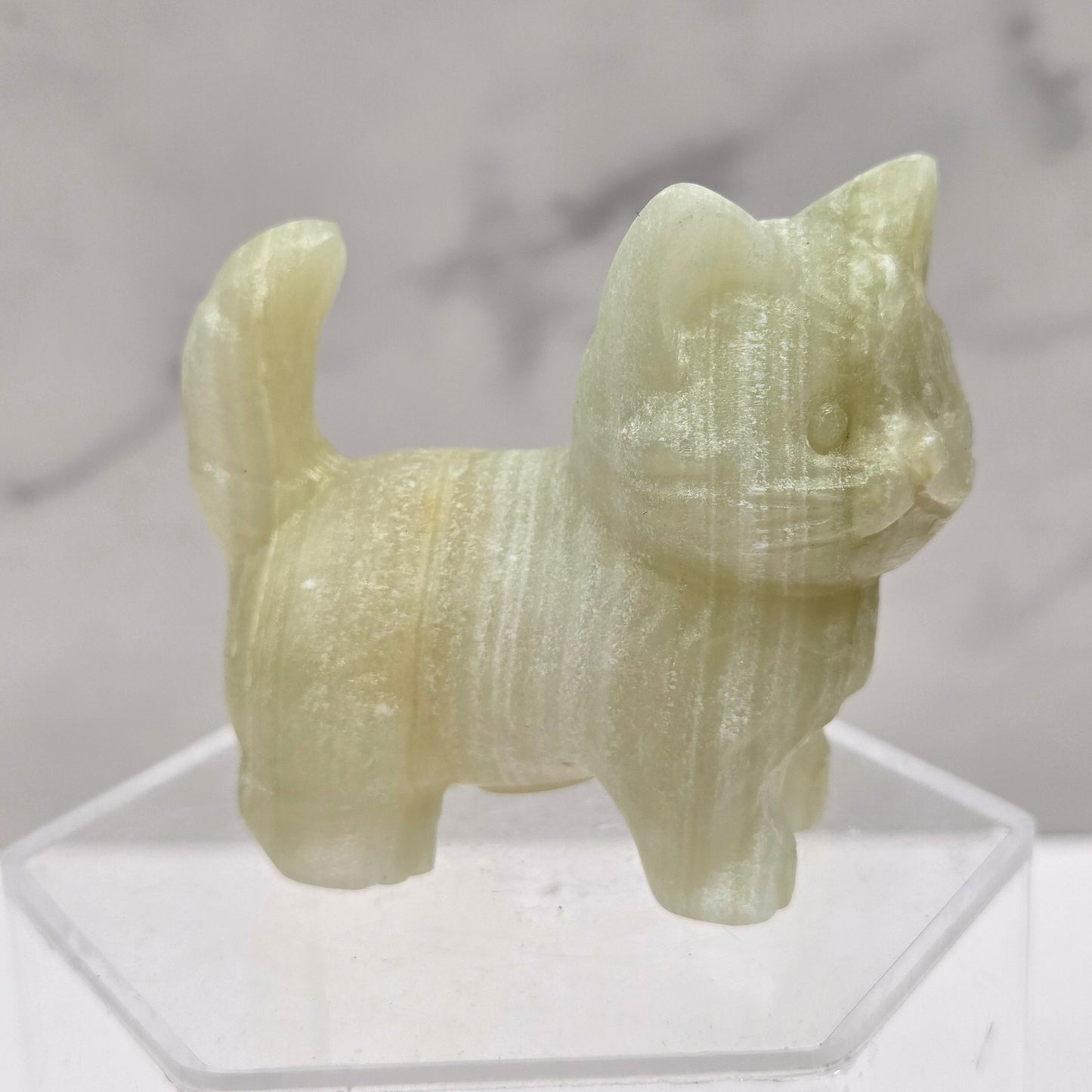 Green stone sculpture of a cat on a clear stand with a marble background