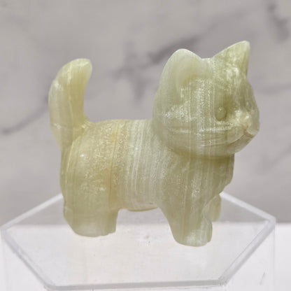 Green stone sculpture of a cat on a clear stand with a marble background