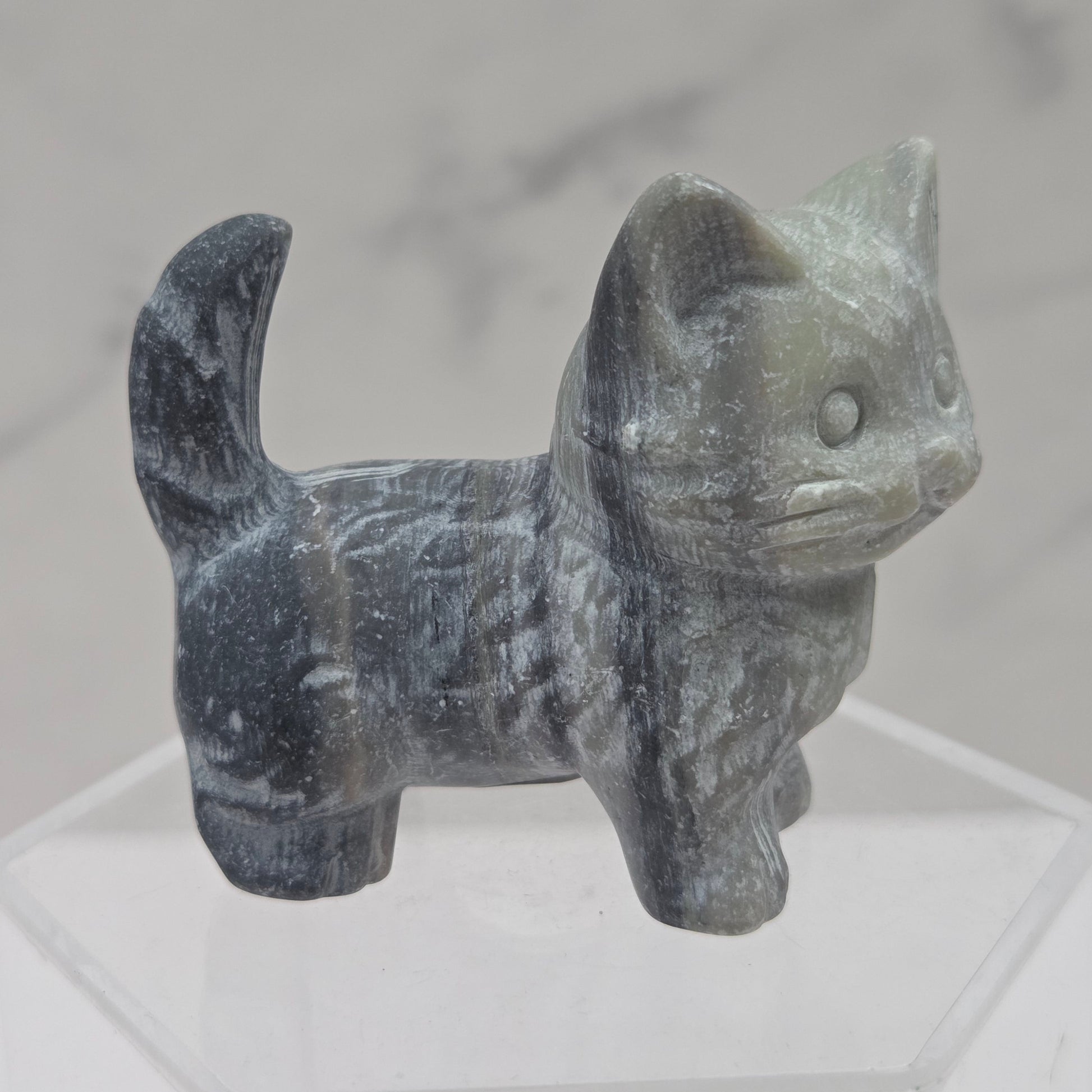 Carved stone cat figurine on a white stand with a marble background