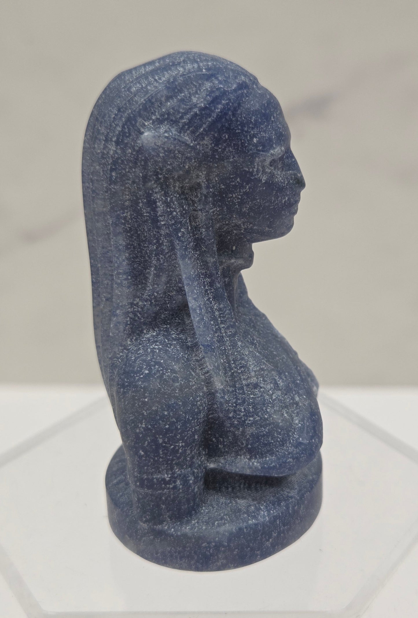 Blue stone sculpture of a figure on a light gray background
