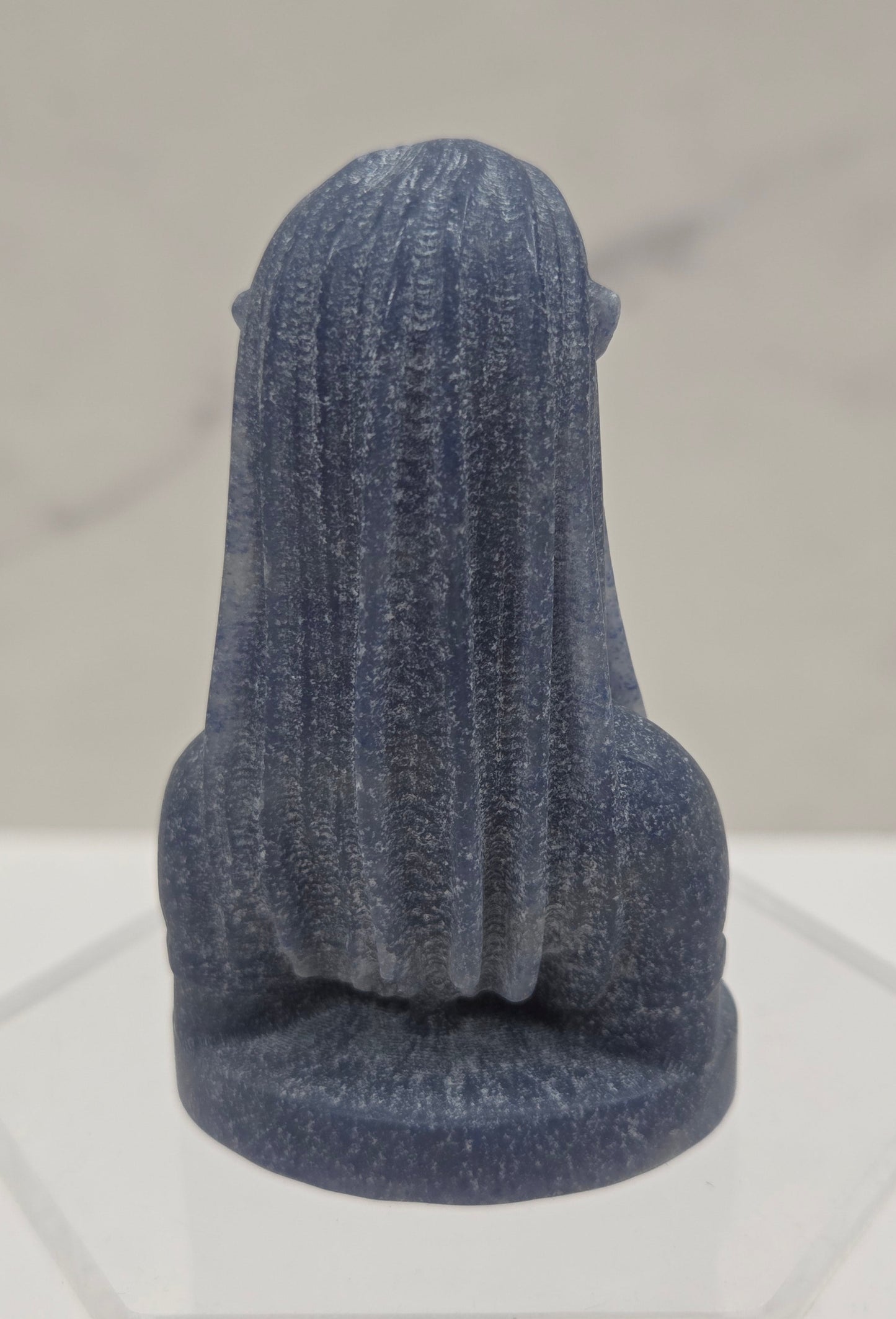 Blue stone sculpture of a figure on a light gray background