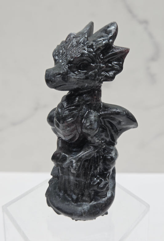 Dragon carving made of garnet sitting on an acrylic stand against a neutral background