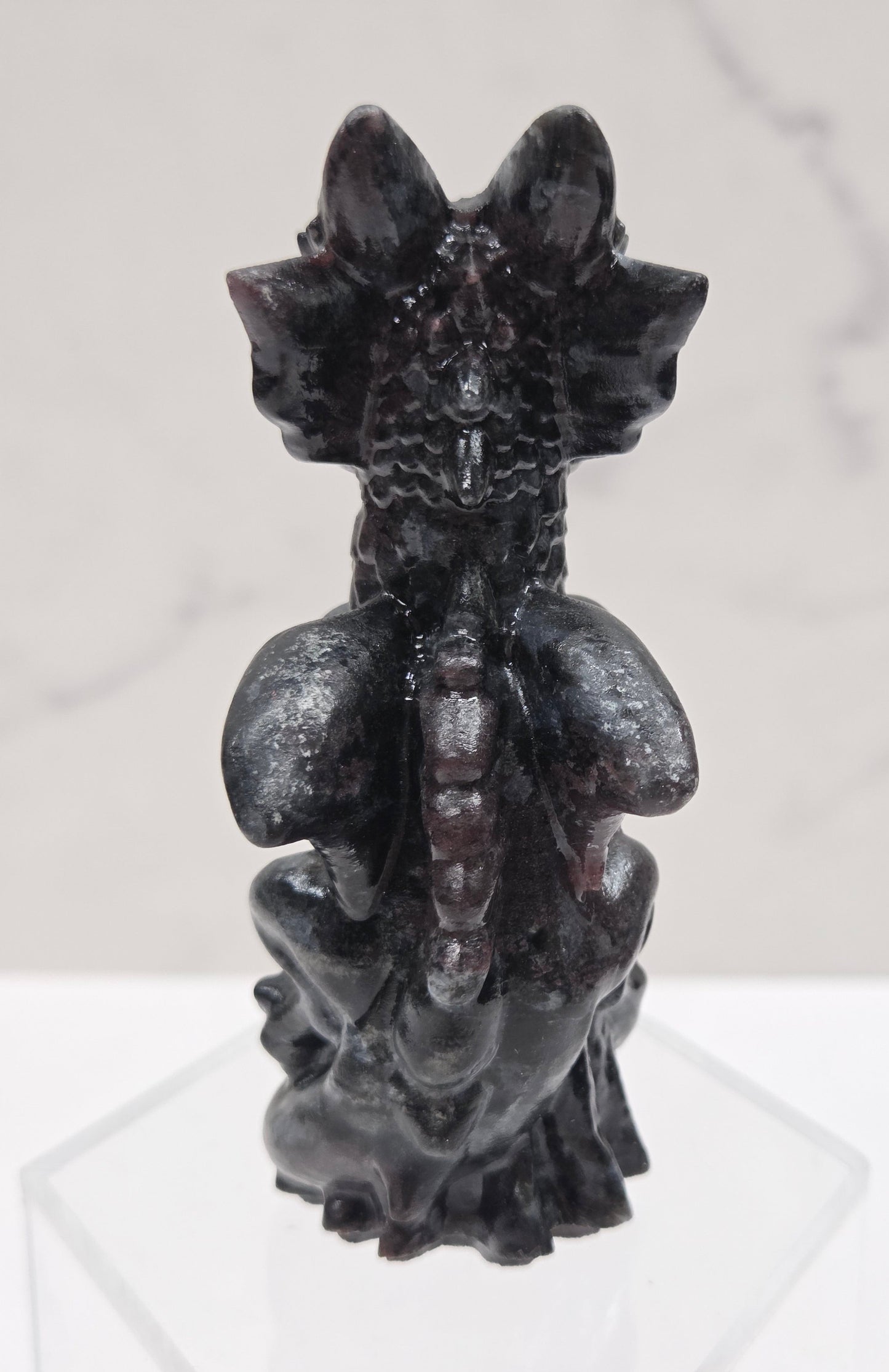 Dragon carving made of garnet sitting on an acrylic stand against a neutral background