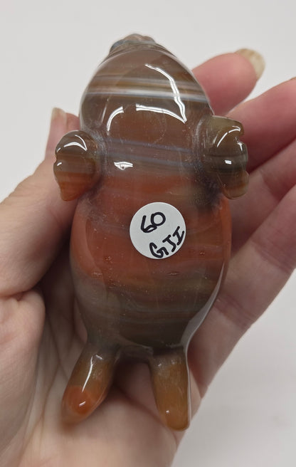 Hand holding a brown and beige crystal sculpture of a walrus with a marble background