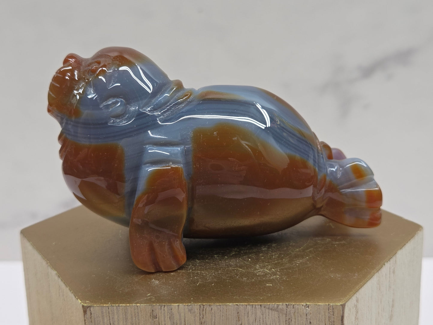 Brown and grey crystal sculpture of a walrus on a hexagonal base with a marble background