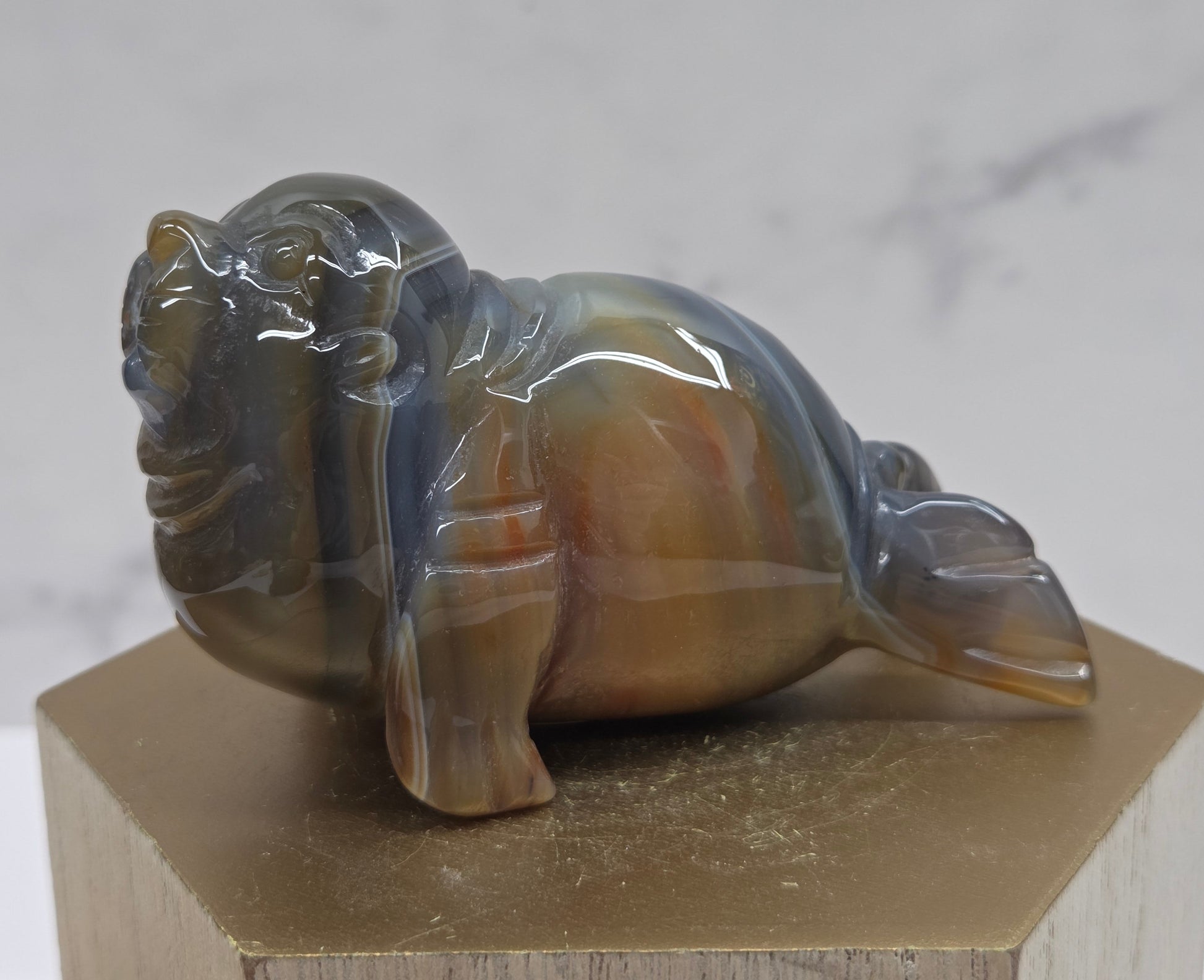 Brown and grey crystal sculpture of a walrus on a hexagonal base with a marble background
