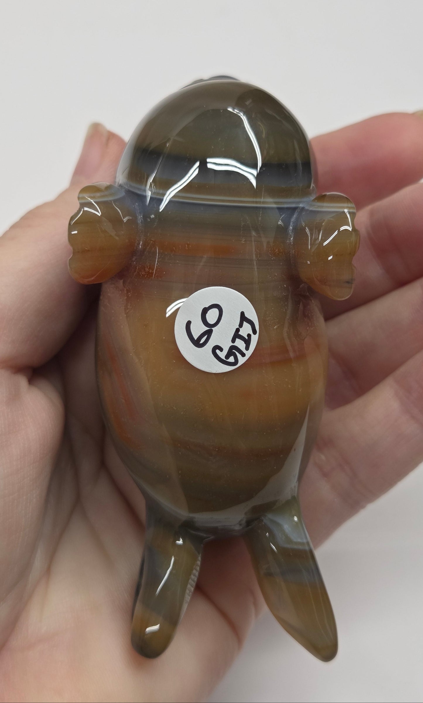 Hand holding a small brown and black figurine with a white label on a plain background