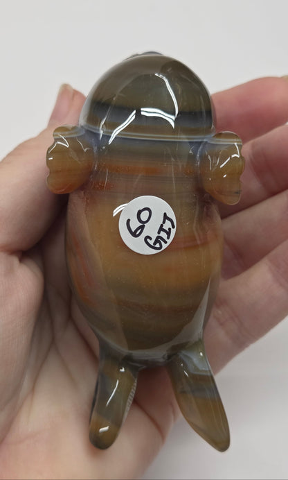 Hand holding a small brown and black figurine with a white label on a plain background