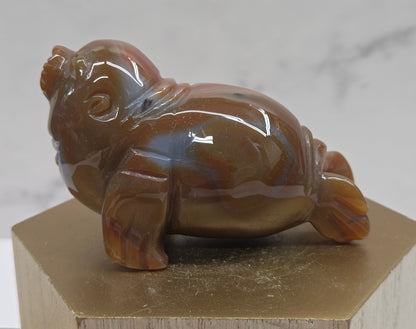 Brown and grey crystal sculpture of a walrus on a hexagonal base with a marble background