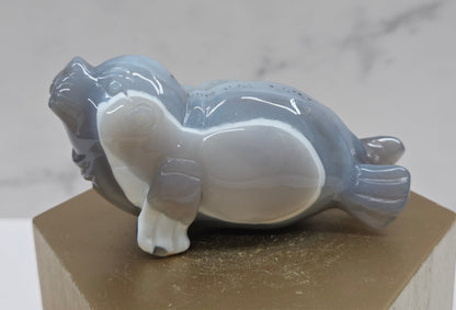 Grey crystal sculpture of a walrus on a hexagonal base with a marble background
