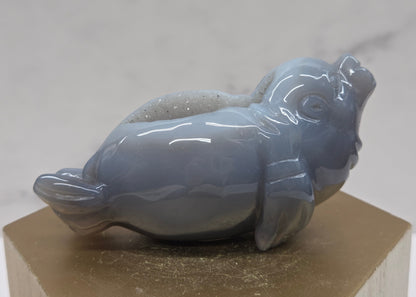 Grey crystal sculpture of a walrus on a hexagonal base with a marble background