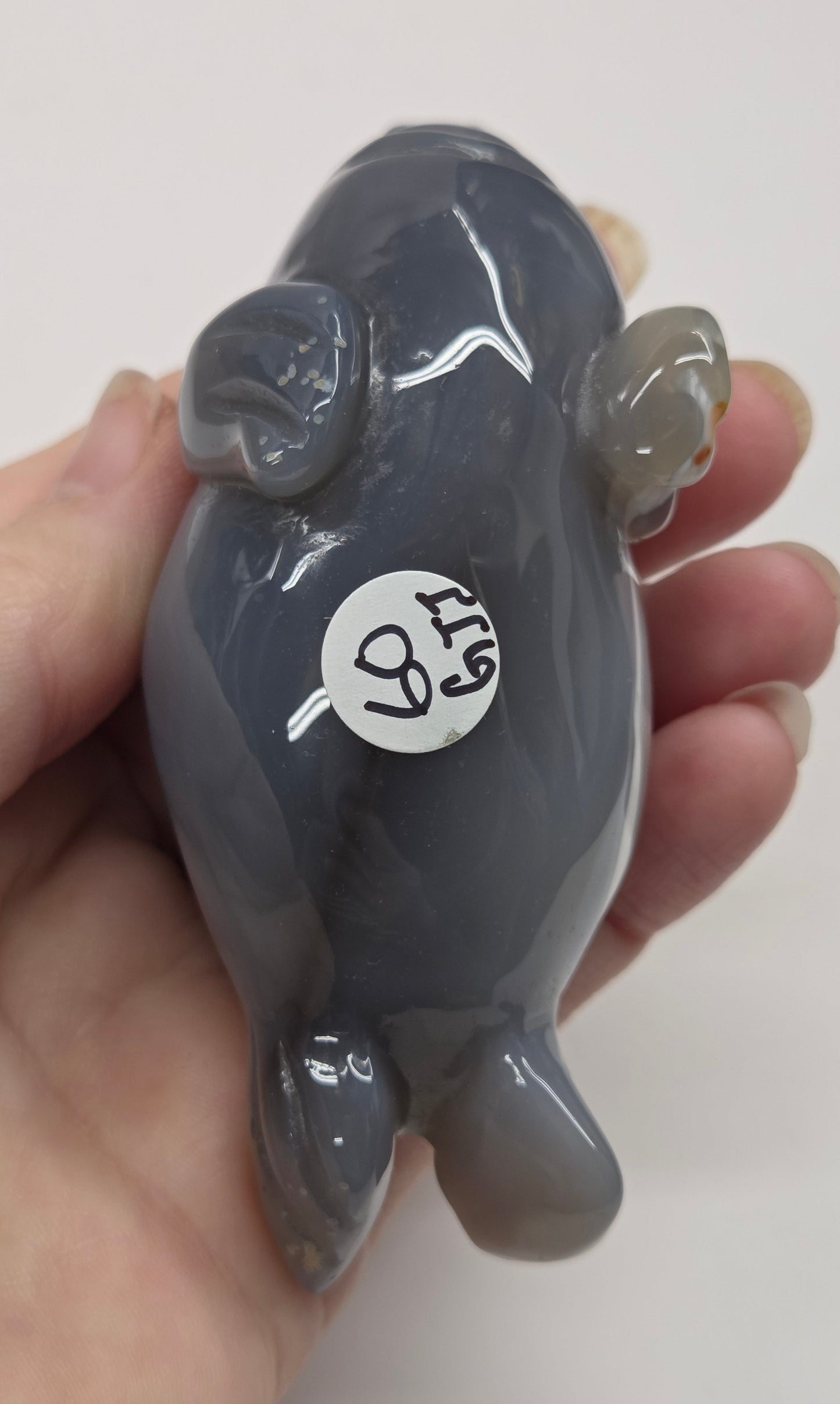 Hand holding a small gray figurine with a white label on a plain background
