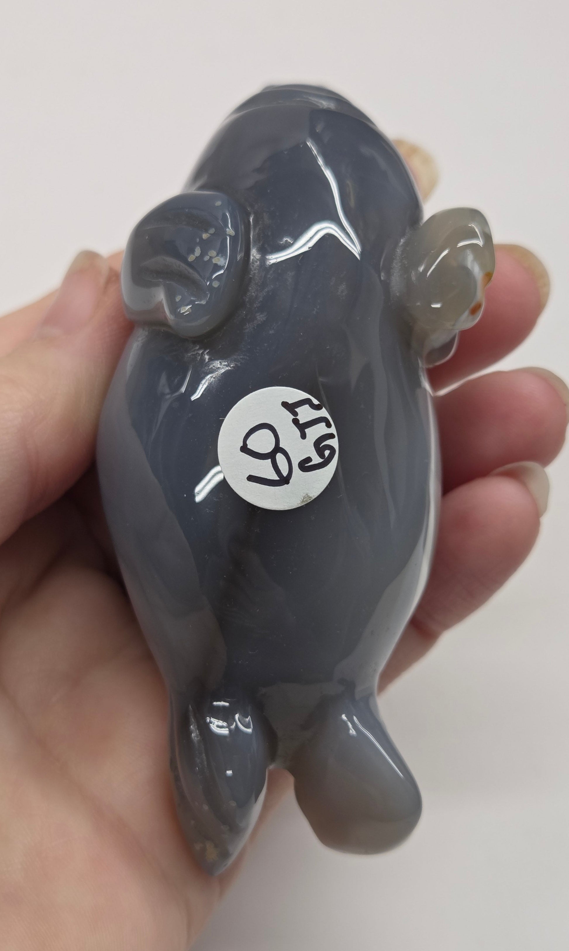 Hand holding a small gray figurine with a white label on a plain background