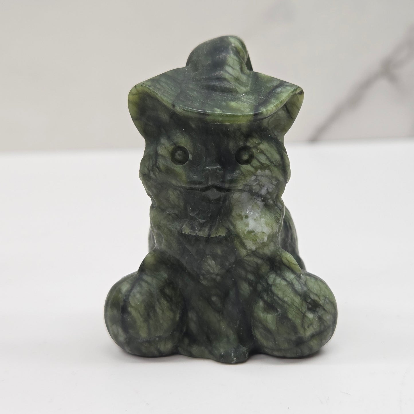 Green jade cat with pumpkin carving on a neutral background