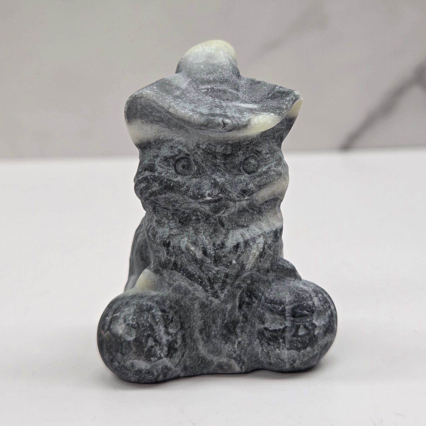 Grey and white stone cat with pumpkin carving on a neutral background