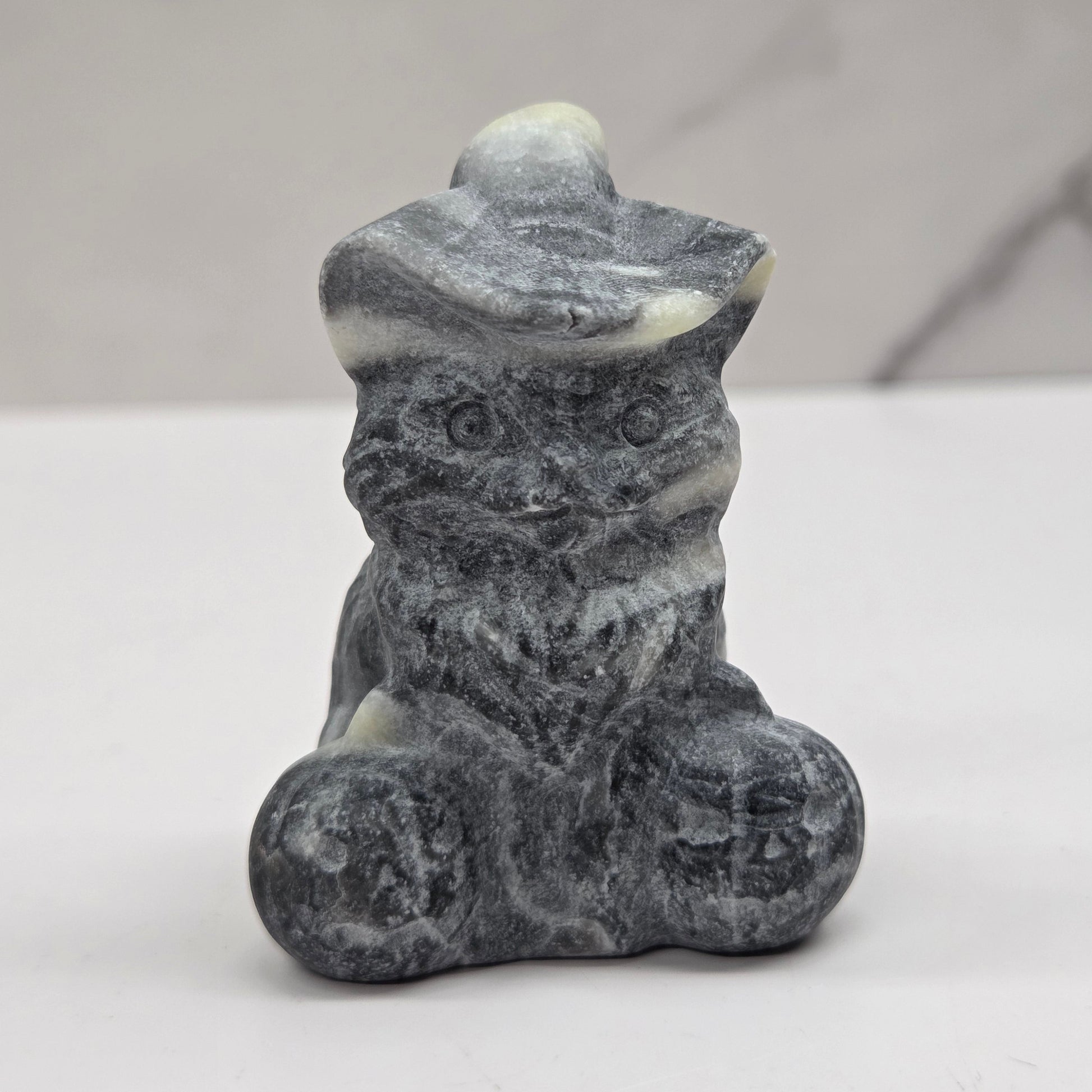 Grey and white stone cat with pumpkin carving on a neutral background