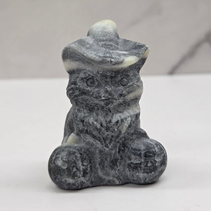 Grey and white stone cat with pumpkin carving on a neutral background