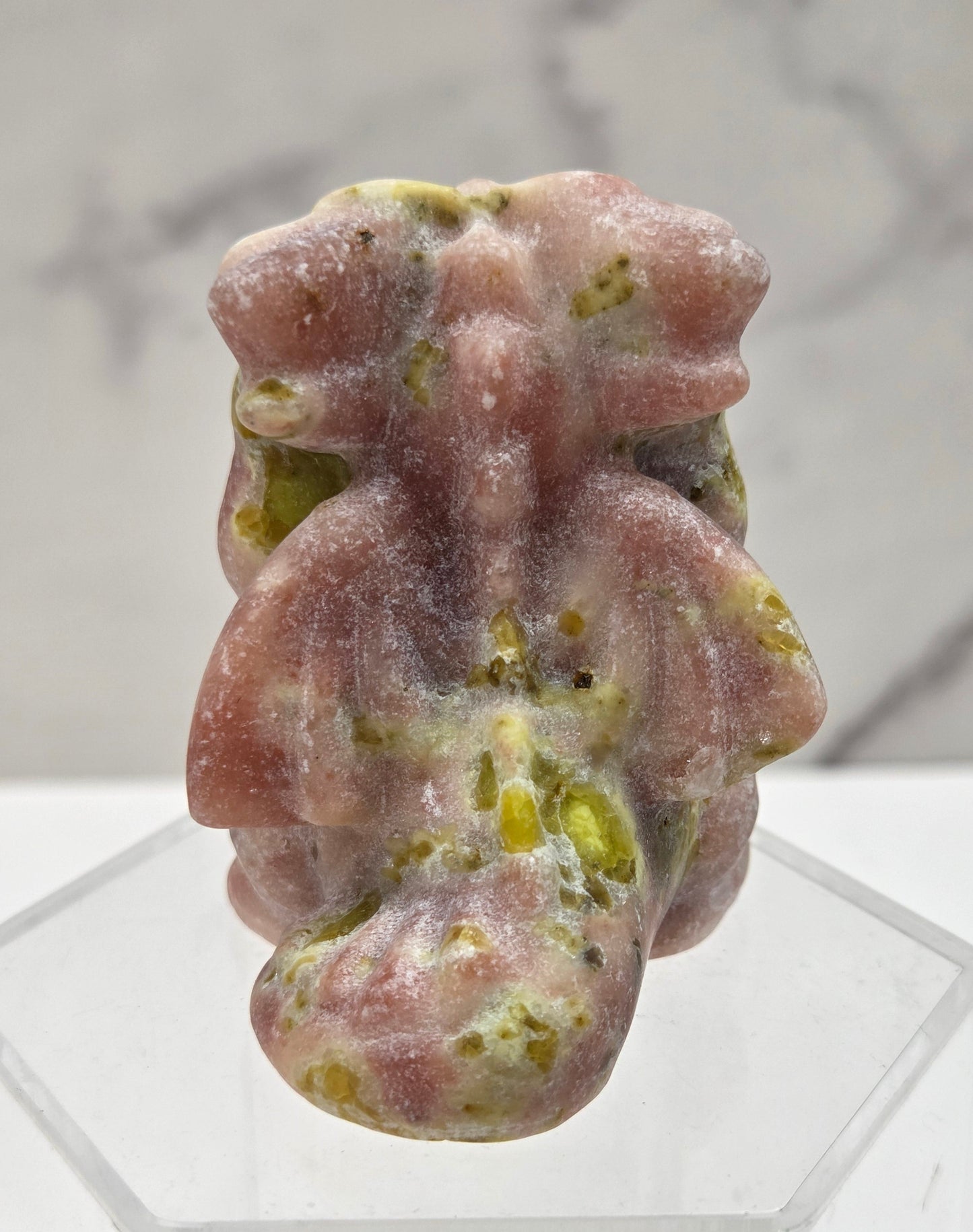 Pink and yellow dragon carving on an acrylic stand against a neutral background