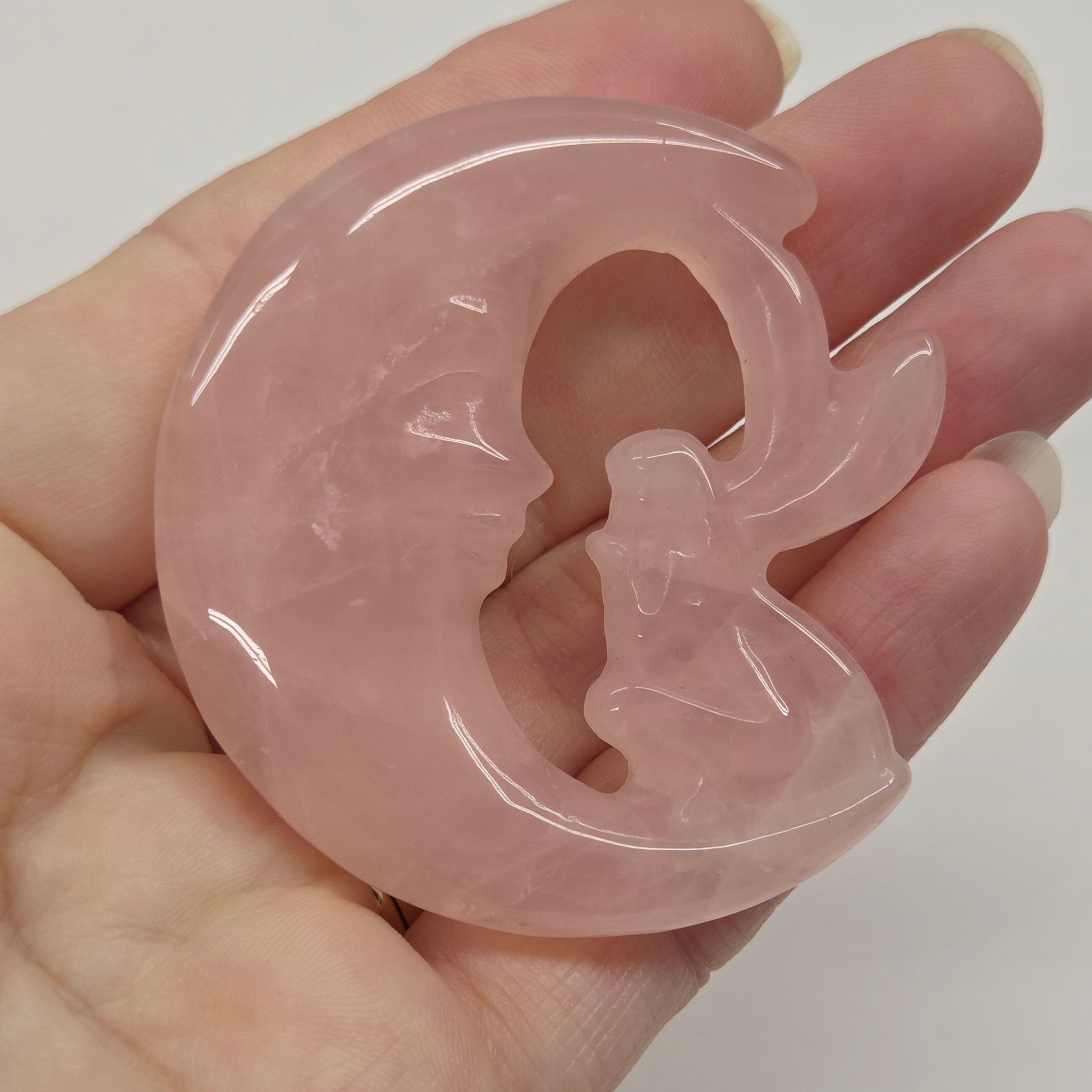 Pink rose quartz fairy on a moon being held in a hand against a neutral background