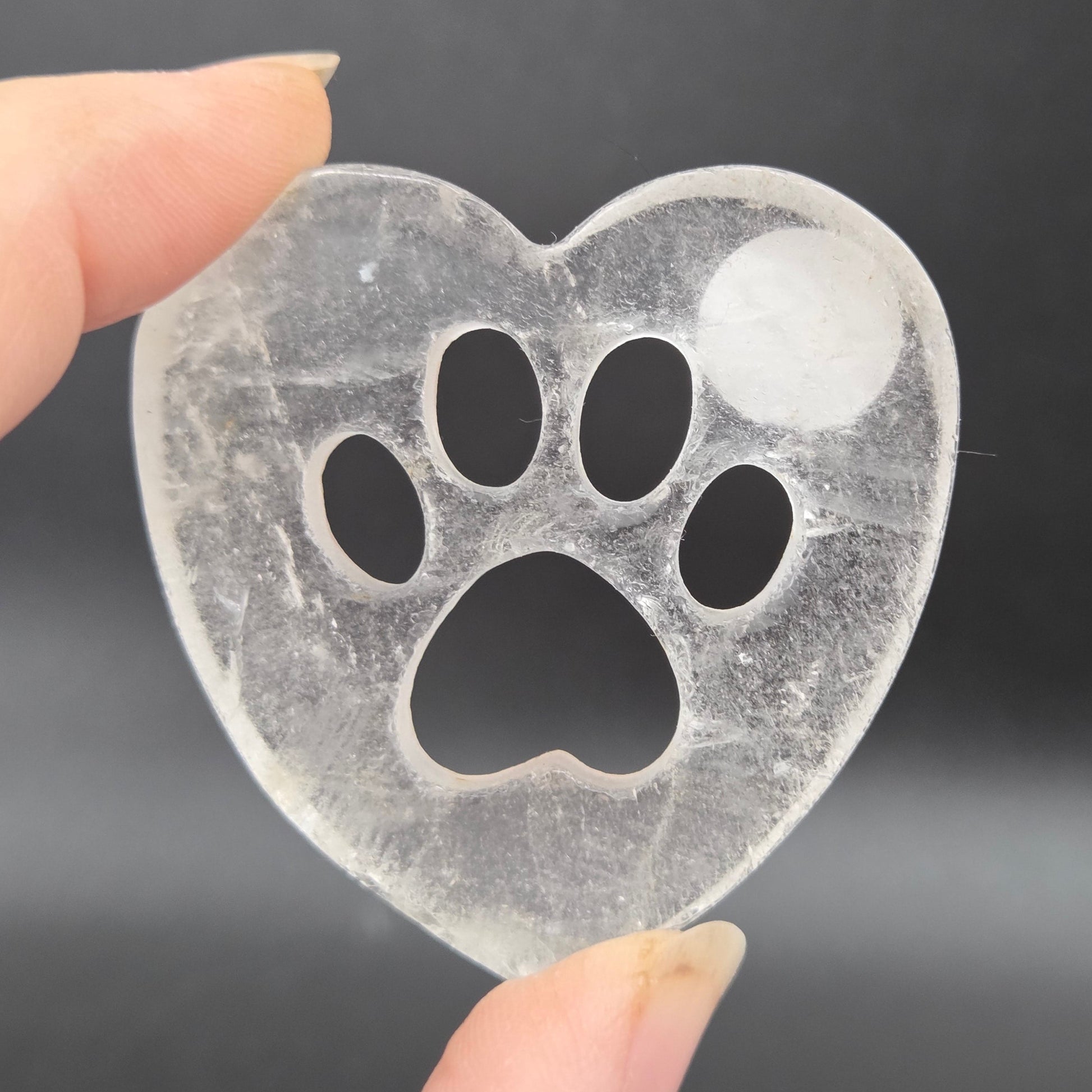 Fingers holding a heart carving with a paw print on a black background