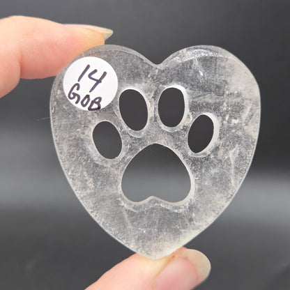 Fingers holding a heart carving with a paw print on a black background